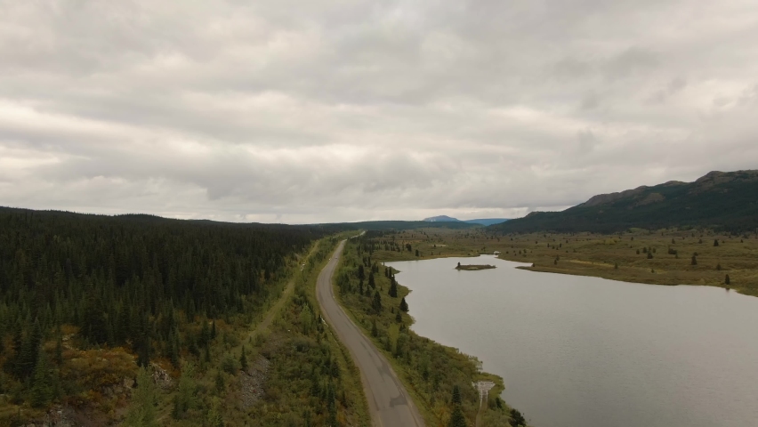 View of Scenic Road alongside Peaceful Lake surrounded by Mountains in Canadian Nature. Aerial Drone Shot. Taken near Stewart-Cassiar Highway, Northern British Columbia, Canada.