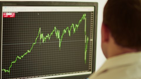 Side view of a young man sitting behind a computer monitor, stock trading