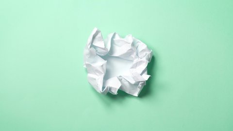 stop motion animation paper wrinkles making a paper ball. Mint green background. A paper ball spreads making a blank sheet and folds again until it disappears.