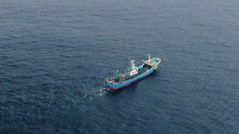 A fishing vessel equipped with a trawl catches fish in the open ocean. Aerial 4K shot.