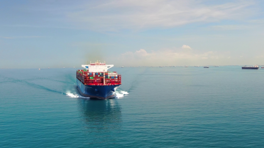 A large container ship for transporting goods near the port of Singapore. A container ship carries cargo across the ocean. Transportation. Delivery. Logistics. Aerial 4K shot.