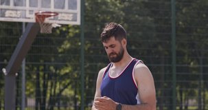 Tired basketball player drinking water at outdoor court, taking break in active game