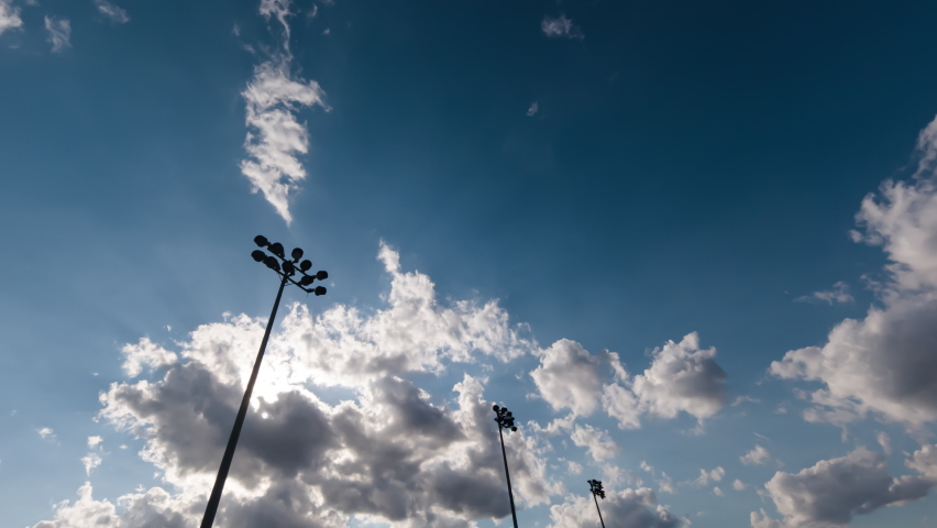 Timelapse with light towers of a football stadium against a sunset and summer clouds, cinematic fast and smooth movement of sky. Soccer stadium flashlights and evening time lapse.