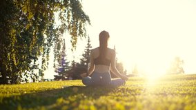 Back view of unrecognizable slender young woman sitting on yoga mat in lotus position and raising hands up outside in city park. Rear view of female practicing yoga outdoors in sunny day. - Powered by Shutterstock - Get 15% off with code: PIKWIZARD15