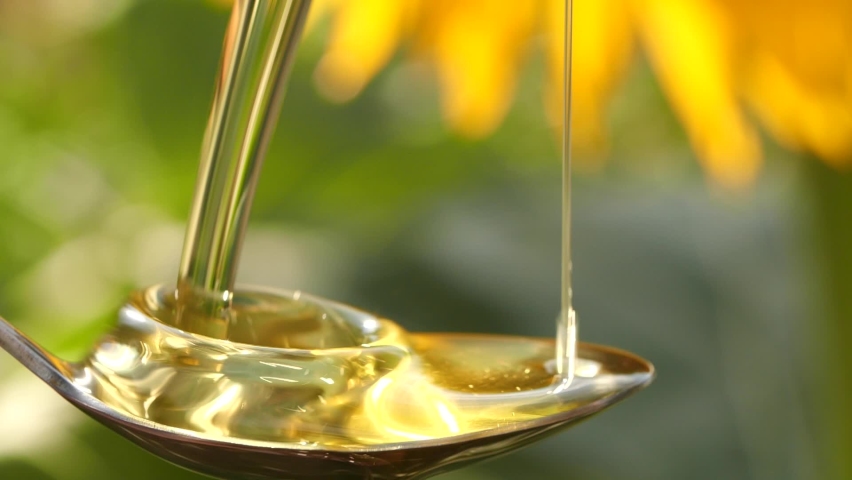 Slow motion of pouring sunflower oil liquid into spoon on nature background