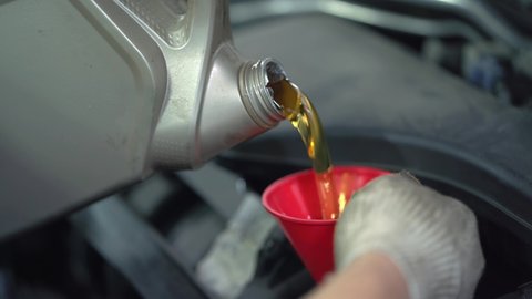 Worker pours new synthetic motor oil from canister into funnel at car service, regular oil change - auto health concept