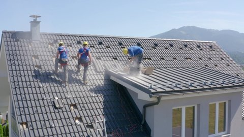 Construction Workers Installing Tiles On Roof Of Suburban House