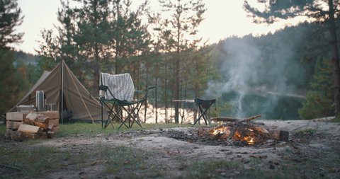 Bonfire burning on beautiful mountain lake shore in tourist camp. Beautiful landscape, campfire, burning wood by tent in summer evening. Active lifestyle, traveling, vacation, hiking, camping concept