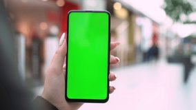 Shopping center. Back view of brunette holding chroma key green screen smartphone watching content. Gadgets and contemporary people concept.