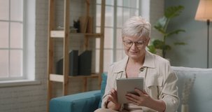 Mature caucasian woman using a tablet computer at home. Senior lady making an order in online store, surfing web 4k footage