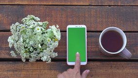 Closeup top view flatlay 4k video of modern mobile smartphone with empty blank green screen lying on wooden brown desk background. Woman scrolls green pages. Banner with copy space. - Powered by Shutterstock - Get 15% off with code: PIKWIZARD15