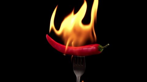 Hot red chili pepper on a fork in flames on a black background. Spicy food concept. Slow motion
