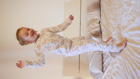 VERTICAL VIDEO - 4 year old Caucasian girl jumps and laughs on the bed in unicorn sleepwear pajamas.