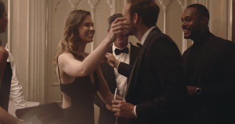 Friends toasting champagne glasses while a couple arriving hand in hand at party. Couple arriving at a party meeting and greeting their friends.
