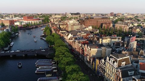 Amsterdam, Netherlands, aerial view of famous places during sunset in spring or summer.  View of canal and old centre district. Munttoren Bell Tower in background. Beautiful warm colors
