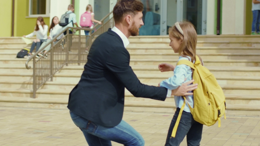 Caucasian father escorts his daughter to school and waving hand saying goodbye. Adorable little child girl hurrying for lessons running to the entrance. Royalty-Free Stock Footage #1059845507