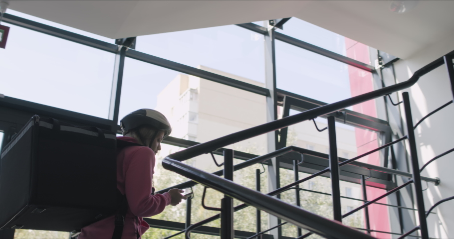 A young female delivery woman courier of a takeaway with isothermal case pizza box goes up the stairs inside the building. 4k raw slow motion footage 50 fps