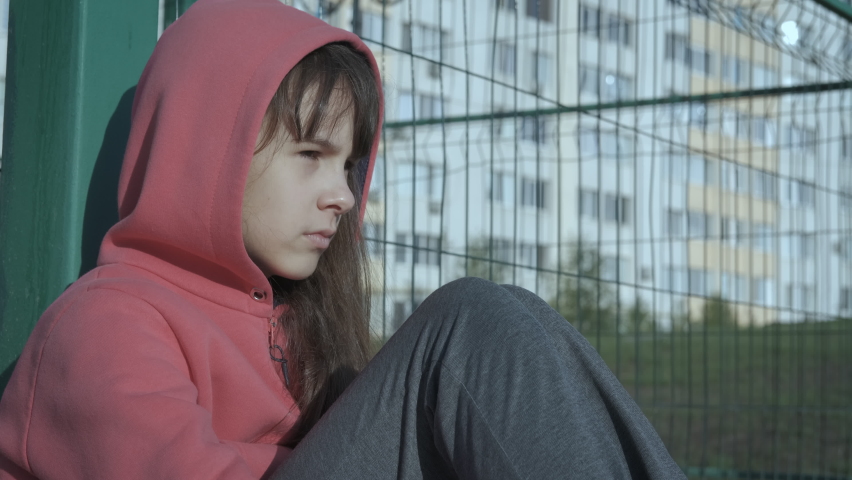 Depressed teenager. Loneliness of a teenager. Sad teenage girl sits by the fence in the yard. | Shutterstock HD Video #1059847388