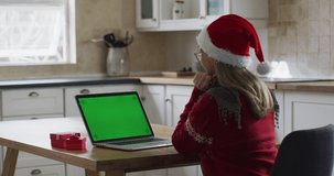 Caucasian woman spending time at home, sitting in kitchen at Christmas
wearing Santa hat, using laptop and opening present. Social distancing
during Covid 19 Coronavirus quarantine, slow motion.