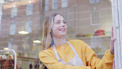 Woman running small business pushing back security grill from window and opening shop viewed from outside - shot in slow motion