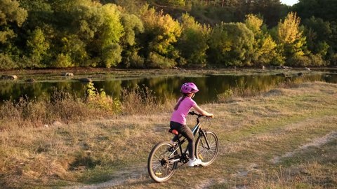 A little girl rides a Bicycle in a protective helmet near river in nature.