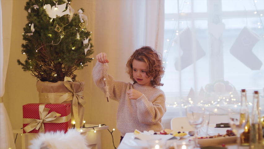 Happy small girl indoors at home, standing by Christmas tree.