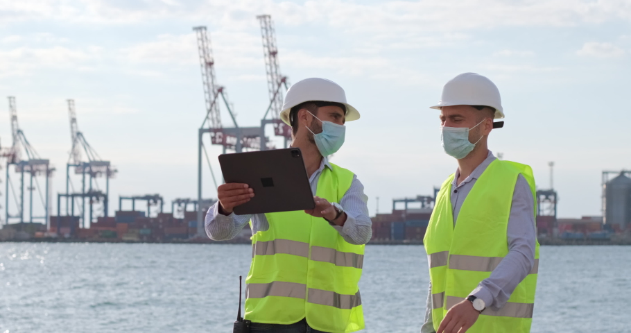 Port workers work with a tablet and point to the object in front of them, standing against the backdrop of marine cranes. Engineers improve seaport logistics. Royalty-Free Stock Footage #1059856931