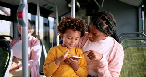 African-american boy playing with phone on mother lap inside bus