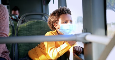 African-american boy with covid mask looking out window inside bus