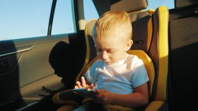 Cute toddler baby boy sitting in car seat and watching a video from smart-phone. Kid playing in the car with smartphone. Technology and internet addiction concept.
