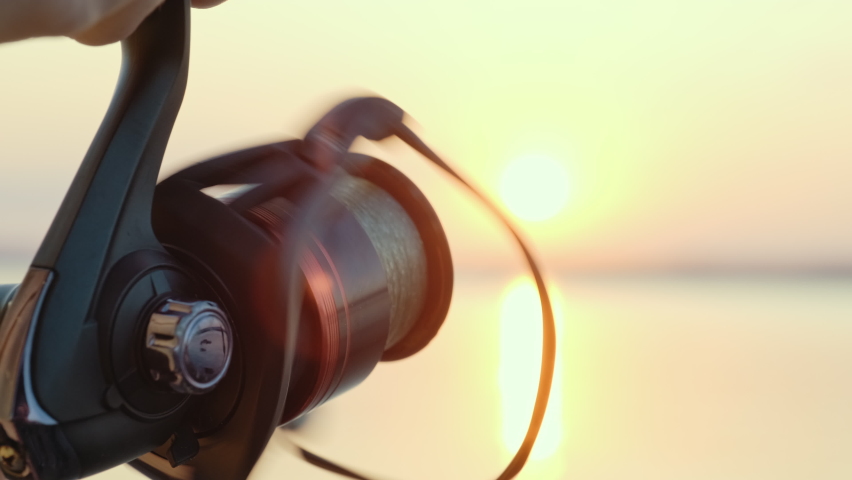 Handle rotation with reel of fishing rod against of orange sunset slow motion. Woman hobby fishing on sea tightens a fishing line reel of fish summer. Lens flare. Calm surface sea. Bright disk of sun Royalty-Free Stock Footage #1059863684