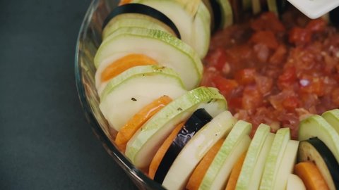 Grease fresh vegatables in the glass bowl with a oil and spices. Cooking delicious healthy vegan meal. Carrots, eggplants, zucchini pieces placed in round form. Making tasty ratatouille with organic