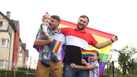 Happy samesex family near their house with flags and two children, a boy and a girl. Gay rights, lgbt community, child adoption, fathers day