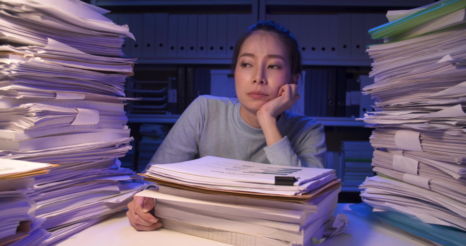 Exhausted asian business woman putting documents on desk cover with stack of paperwork. Tired alone girl looking at paper and lay down on pile of sheets while working hard at late night at home. | Shutterstock HD Video #1059865640