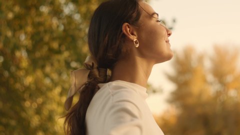 Portrait of an attractive brunette woman walking in the park at fall on a sunny day and smiling. The face of a happy beautiful woman in autumn outdoor. Slow-motion 4k footage