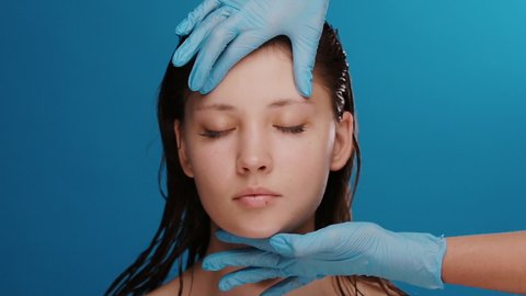 plastic surgeon checking and measuring woman face before operation on blue background, cosmetology doctor in blue gloves examing female before surgery