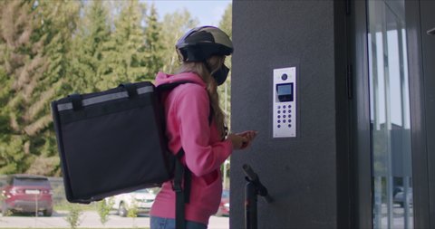Female courier with isothermal food case box arrives on a electric scooter to the entrance to the house and calls the intercom. Deliverman deliver orders. 4k raw slow motion footage 50 fps