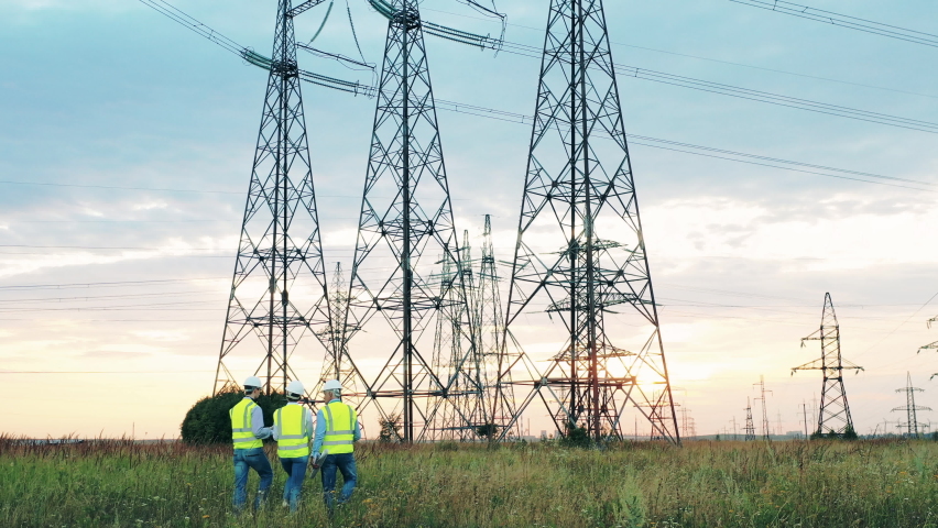 Field with power pylons and energetics workers walking across it Royalty-Free Stock Footage #1059870353