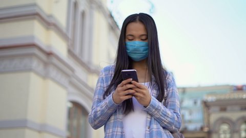 young woman student asian in medical mask. woman looks at a smartphone and scrolls through social media. 4K