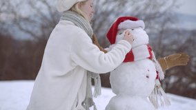 Closeup of a cheerful young woman by snowman on snow hill. Funny snow man with carrot nose. Winter fun and leisure vacation - Powered by Shutterstock - Get 15% off with code: PIKWIZARD15
