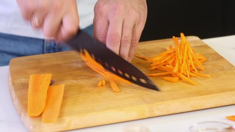 Chef cuts carrots for salad with a sharp knife. male chef prepares salad in the kitchen at home. Cooking a delicious meal in the restaurant kitchen. Preparation of ingredients. Healthy food every day