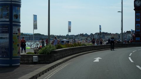 WEYMOUTH, ENGLAND, UNITED KINGDOM - AUGUST, 2020: Car front view driving The Esplanade in English seaside resort Weymouth town. People on the beach and in the sea enjoying hot summer day.