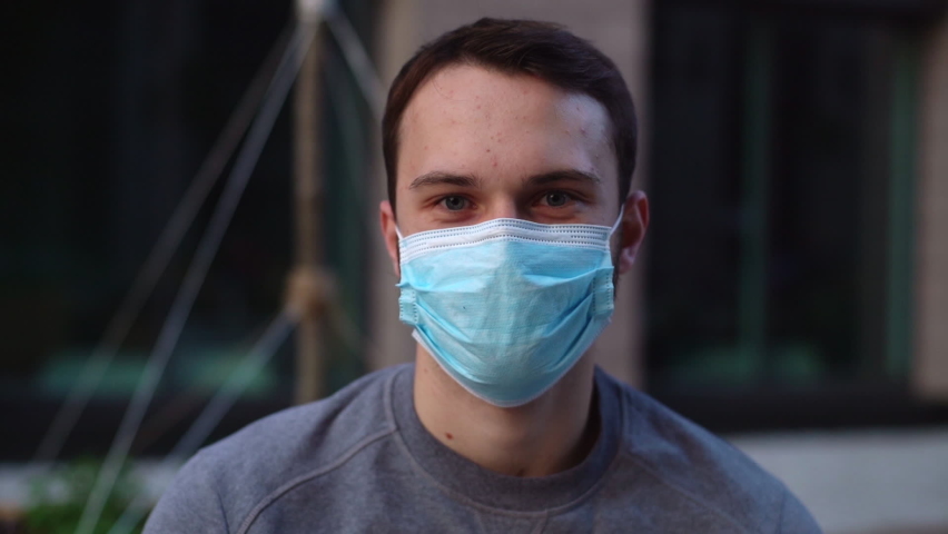 Close-up face of cheerful young man take off medical mask and smiling looking at the camera. Portrait of handsome bearded male removing protective mask and looking with positive emotion at city street Royalty-Free Stock Footage #1059878426