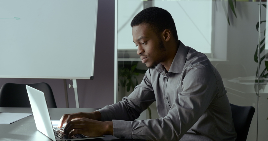 Portrait of one young African man typing on laptop sitting in office writing notes in notebook, serious american businessman working with technology indoor, black adult student study online in net Royalty-Free Stock Footage #1059879278