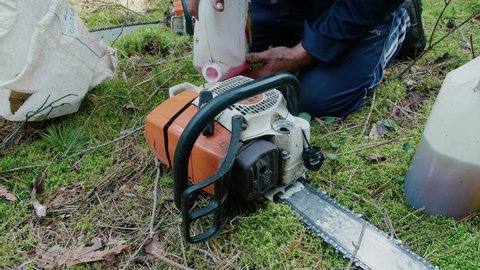 A man fills up gasoline and prepares a chainsaw for work in the forest. Petrol Chainsaw.