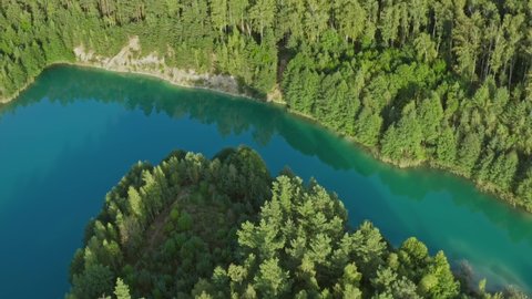 Aerial top view amazing blue lake surrounded by green pine forest. Curved lakeshore and clean turquoise water. Pond in woodland. Golden hour, warm sunlight during sunset or sunrise