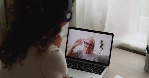 Young and mature women talking through videocall application, laptop screen view over female shoulder. Family living at distance call up using videoconference app, remote talk, virtual meeting concept