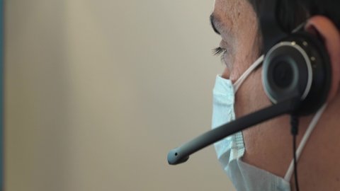 Close-up of a man in a medical mask talking on a headset in an office. Portrait of a male call center operator during a virus outbreak. Business worker answer customer calls during outbreak covid