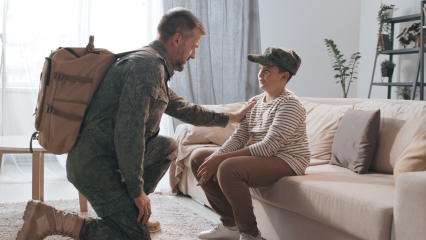Medium shot of male army officer in military uniform kneeling before his son and saying goodbye to him before leaving for deployment Royalty-Free Stock Footage #1059883793