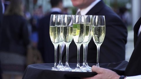 Waiter offer a glass of champagne on a tray. Fine classy champagne is served during a ceremony. Slowmotion